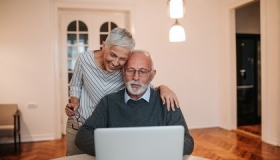 Altes Ehepaar sitzt vor Laptop und plant seinen Hausverkauf und danach darin wohnen zu bleiben.